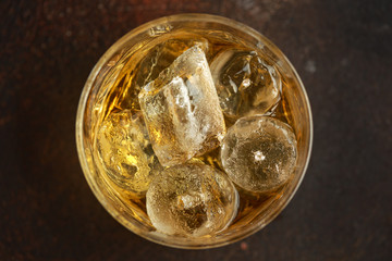 Glass of whiskey with ice on rustic wooden table