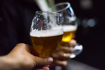 Close-up view of a two glass of beer in hand. Beer glasses clinking in bar or pub
