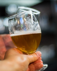 Close-up view of a two glass of beer in hand. Beer glasses clinking in bar or pub