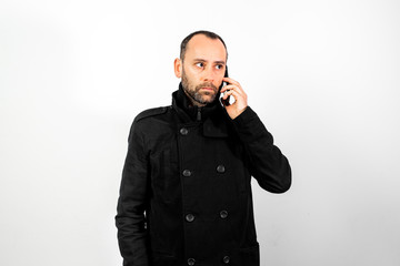 Middle-aged man with overcoat listens attentively to a conversation on his mobile phone, isolated on white.