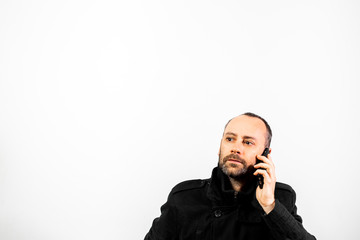 Middle-aged man with overcoat listens attentively to a conversation on his mobile phone, isolated...