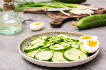 Fresh cucumber salad, boiled chicken eggs and green onions on a plate and ingredients for cooking on the table