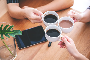 Top view image of three people clinking coffee cups on wooden table in cafe