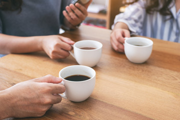 Closeup image of people using mobile phone and drinking coffee together