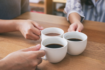 Fototapeta na wymiar Closeup image of three people holding and clinking coffee cups to drink on wooden table