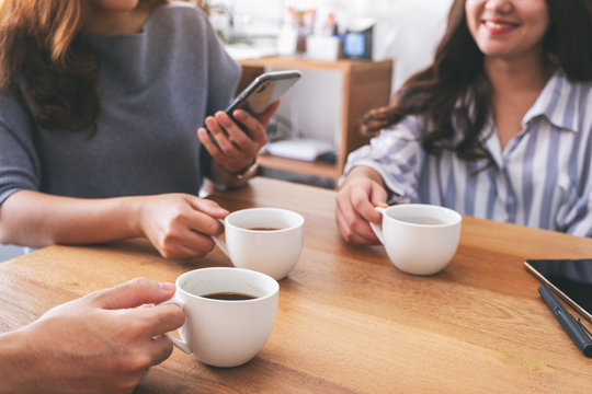 Closeup image of people using mobile phone and drinking coffee together