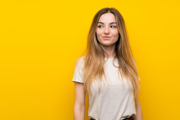 Young woman over isolated yellow wall standing and looking to the side