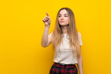 Young woman over isolated yellow wall touching on transparent screen