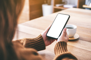 Mockup image of a woman holding black mobile phone with blank desktop screen with coffee cup on the...