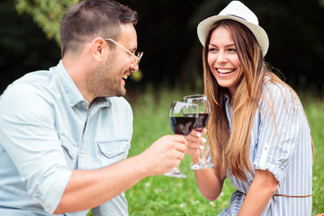 Happy young couple celebrating anniversary or birthday with a wine toast. Relaxing picnic in a park