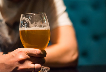 man's hand holds a glass of beer in bar