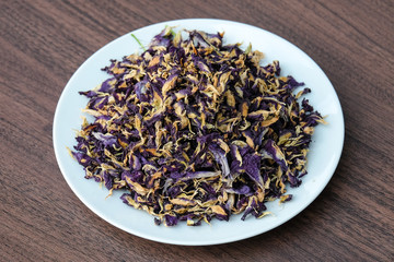 Dry pea flowers on white plate, wooden table for nature background or texture - violet concept.