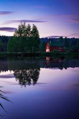 Small village house and trees reflects in still water at beautiful evening
