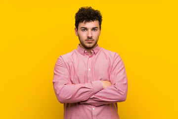 Man with curly hair over isolated yellow wall keeping arms crossed