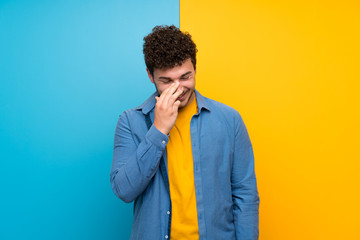 Man with curly hair over colorful wall smiling a lot