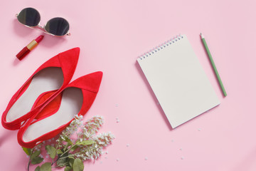 Fashion blog spring style desk with woman accessory collection: red high heel shoes, scarlet lipstick, mirrored sunglasses, notebook and bird cherry branch on pastel pink background. Flat lay.Top view