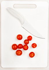 Fototapeta na wymiar modern plastic white cutting board with white knife and red cherry tomatoes like a graphic background with copy space vegetables 
