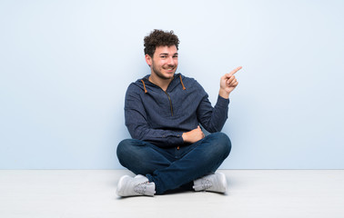 Young man sitting on the floor pointing finger to the side