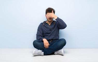 Young man sitting on the floor covering eyes by hands. Do not want to see something