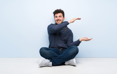 Young man sitting on the floor holding copyspace to insert an ad