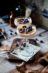 Two champagne glasses with caramel colored panna cotta, jelly, mousse or pudding with chocolate and blueberries on top stands on wooden board