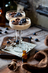 Two champagne glasses with caramel colored panna cotta, jelly, mousse or pudding with chocolate and blueberries on top stands on wooden board