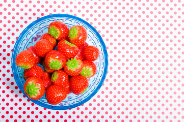 blue glass bowl with fruit red strawberries over background with polka dots and copy space
