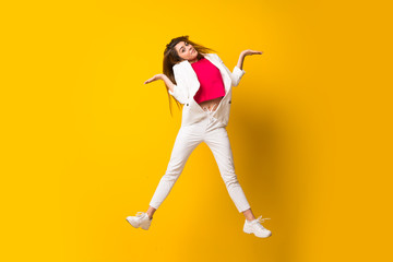 Fototapeta na wymiar Young woman jumping over isolated yellow wall having doubts