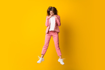 Fototapeta na wymiar Young woman jumping over isolated yellow wall doing surprise gesture