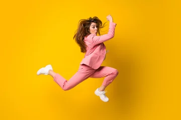 Tuinposter Young woman jumping over isolated yellow wall © luismolinero