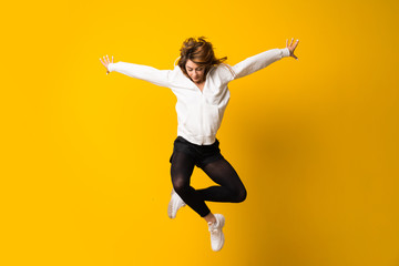 Young woman jumping over isolated yellow wall