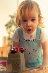 Little smiling girl playing with sand castle and red car toy in sandbox