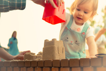 Little smiling girl building sand castle in sandbox in summer