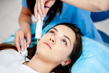 cosmetologist with a patient during facial procedures in a modern cosmetological and aesthetic clinic. A patient receives an electric facial massage. Skin rejuvenation and wrinkle smoothing.