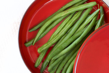 Raw green beans on a red plate.