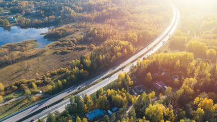 Aerial view of road in beautiful autumn forest. Beautiful landscape with asphalt rural road, trees with red and orange leaves. Highway through the park. Top view from flying drone. 
