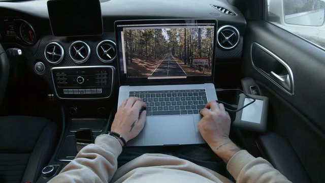 POV shot of blogger or freelance creative professional work remotely from office on laptop on car passengers seat, goes through social media content, videos and photos. Concept nomad lifestyle