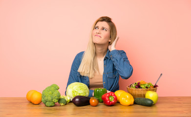 Young blonde woman with many vegetables having doubts