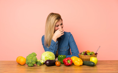 Young blonde woman with many vegetables smiling a lot