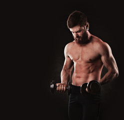 Young strong man bodybuilder on the black background. Dark dramatic colors.