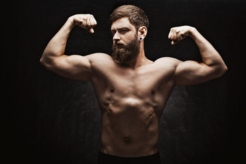 Obraz premium Young strong man bodybuilder on the black background. Dark dramatic colors.