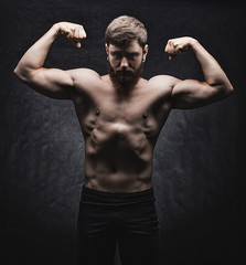 Young strong man bodybuilder on the black background. Dark dramatic colors.