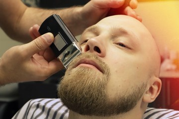 Barber shaves beard of client man on chair Barbershop. Beard Haircut. barber shaving beard with...