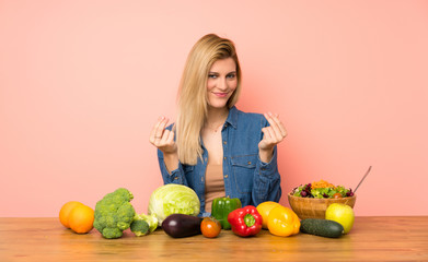 Young blonde woman with many vegetables making money gesture