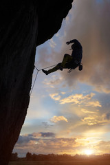 Low angle view of athletic male silhouette abseiling from steep rocky wall in valley at sunset....