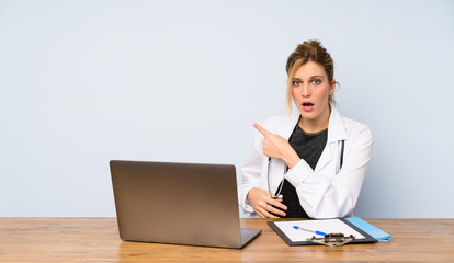 Blonde doctor woman surprised and pointing side