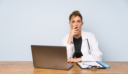 Blonde doctor woman surprised and shocked while looking right