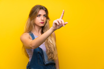 Young blonde woman with overalls over isolated yellow background touching on transparent screen