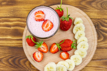 Glass of fresh smoothie of strawberry and banana on a wooden table. Top view