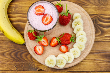 Glass of fresh smoothie of strawberry and banana on a wooden table. Top view
